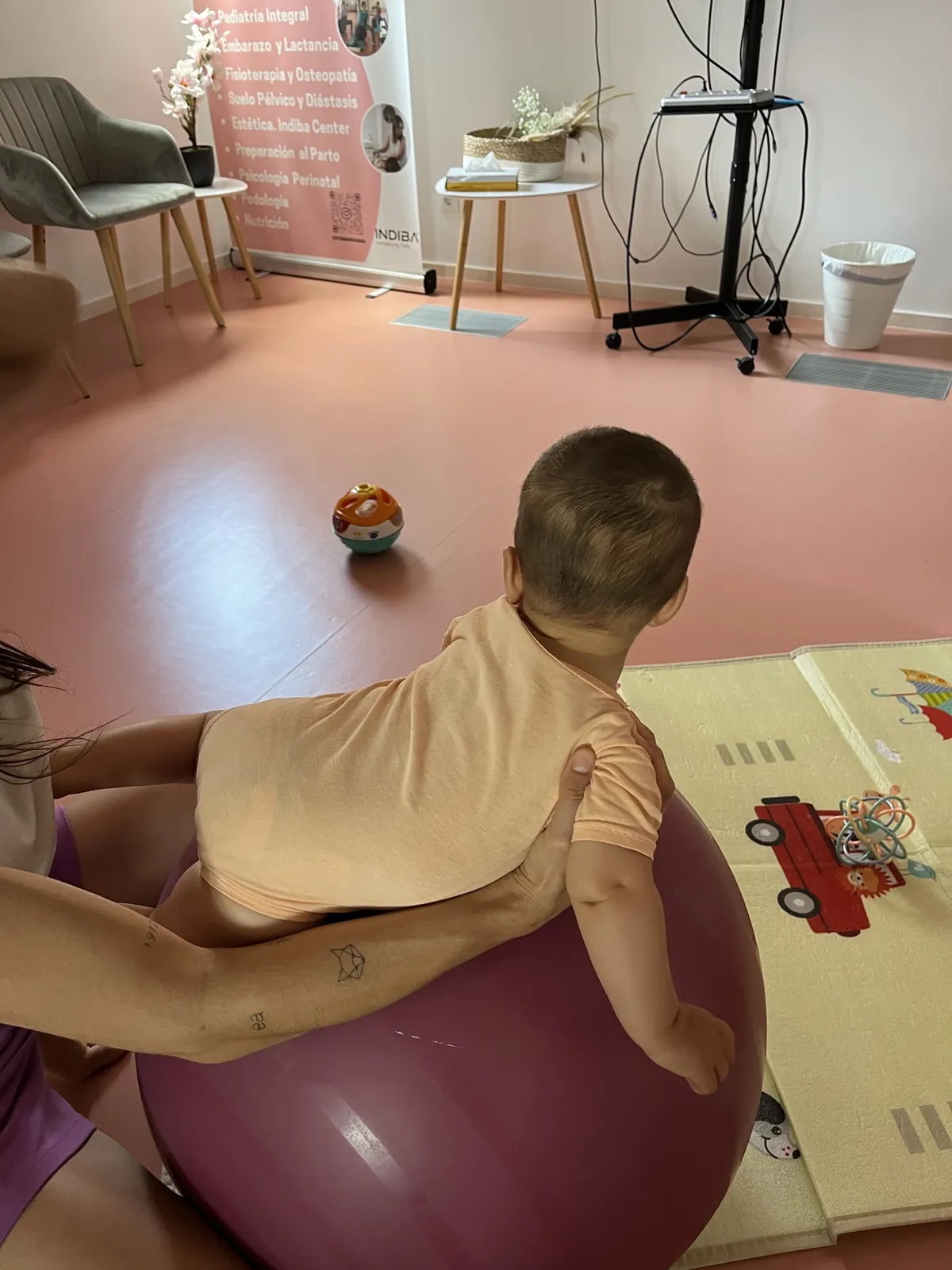 Bebé boca abajo sobre una pelota trabajando el control de cabeza y tronco con la fisioterapeuta