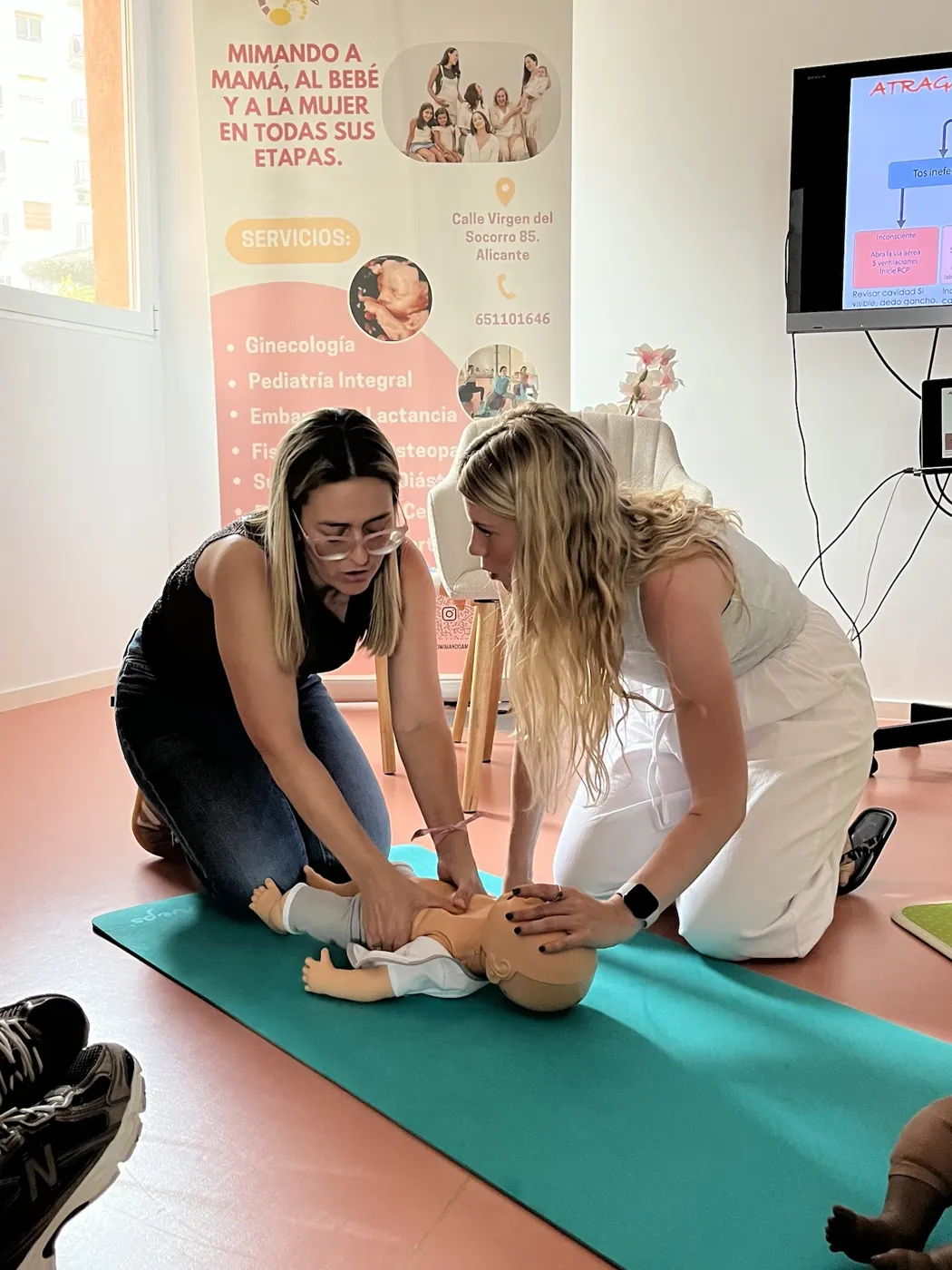 Dos madres practicando RCP con un maniquí de bebé en el taller de primeros auxilios pediátricos de Mimando a Mamá en Alicante