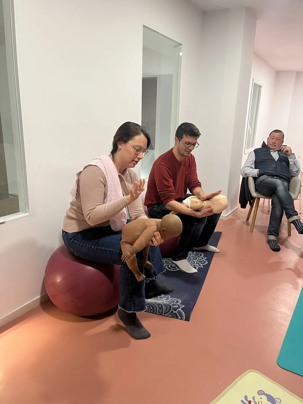 Pareja practicando golpes en la espalda y compresiones con maniquíes de bebé en el taller de primeros auxilios pediátricos de Mimando a Mamá en Alicante