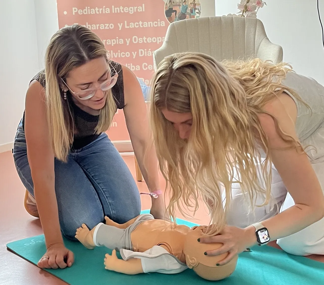 Dos madres practicando RCP con un maniquí de bebé en el taller de primeros auxilios pediátricos de Mimando a Mamá en Alicante